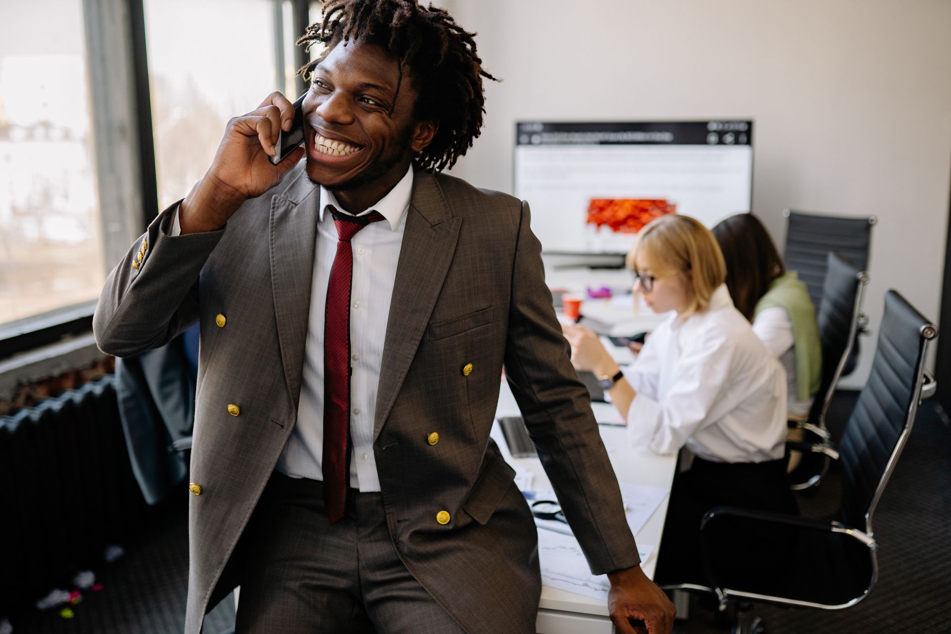 Confident businessman with dreadlocks smiling while on a phone call in a modern office setting.