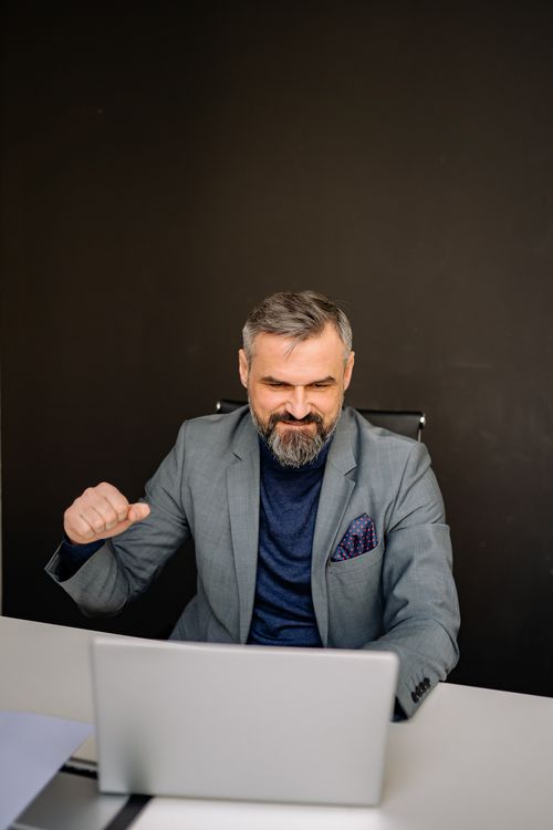 Free Confident businessman in a suit celebrating a victory in modern office setting. Stock Photo