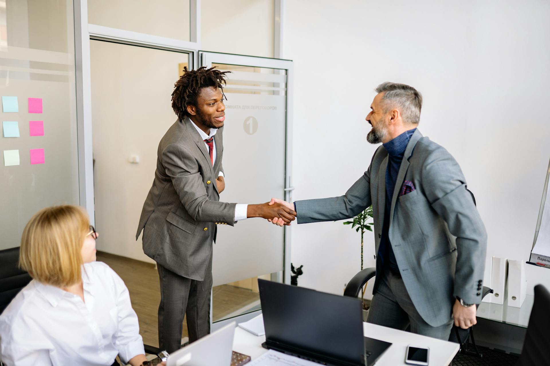 Two businessmen shaking hands in a modern office setting, symbolizing agreement.