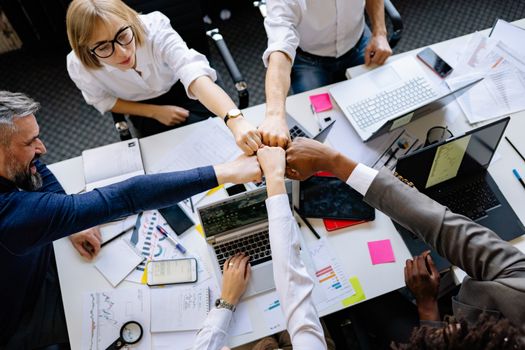 Creative team unites with a fist bump signifying collaboration in an office setting.