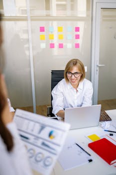 Businesswoman in glasses working on a laptop in a modern office setting with colorful sticky notes.