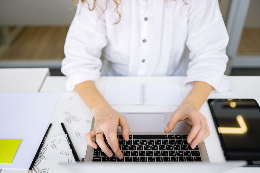 Close-up of woman's hands typing on laptop keyboard in bright, modern office space. Ideal for work and technology themes.