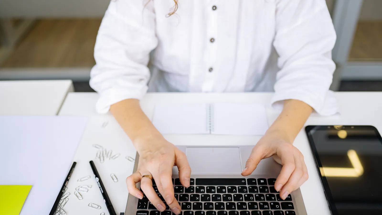 Woman typing on a laptop at a desk with a notebook beside her