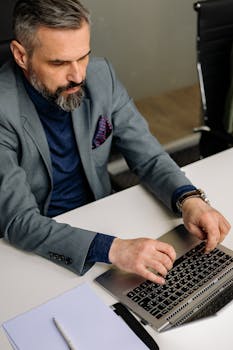 Confident businessman in a suit typing on a laptop at his office desk.