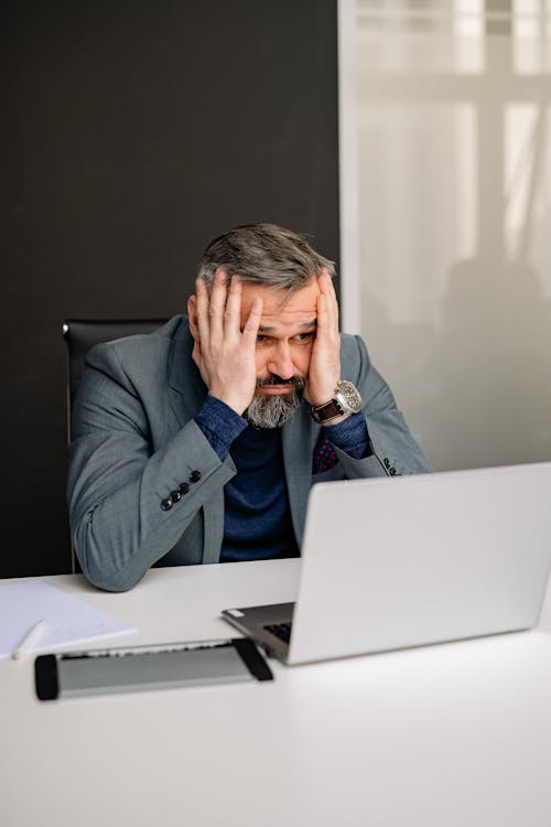 Man with His Hands on His Face While Looking at the Screen of a Laptop