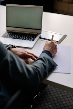 Professional working on documents beside a laptop in a modern office.