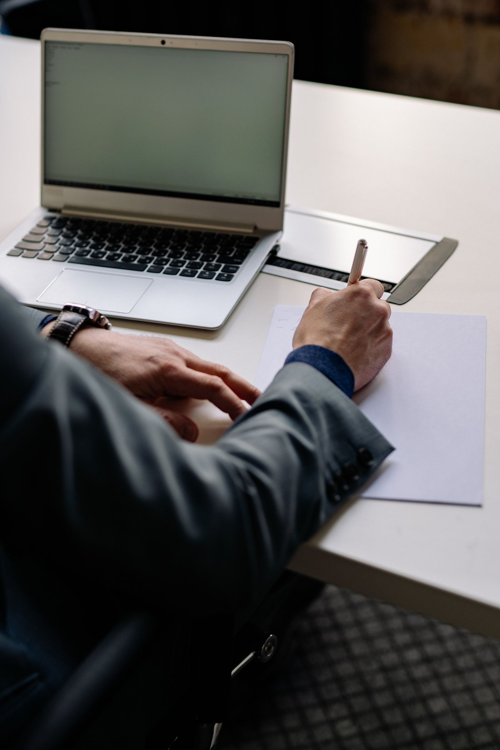 Professionnel rédigeant des notes à côté de documents et d’un ordinateur portable