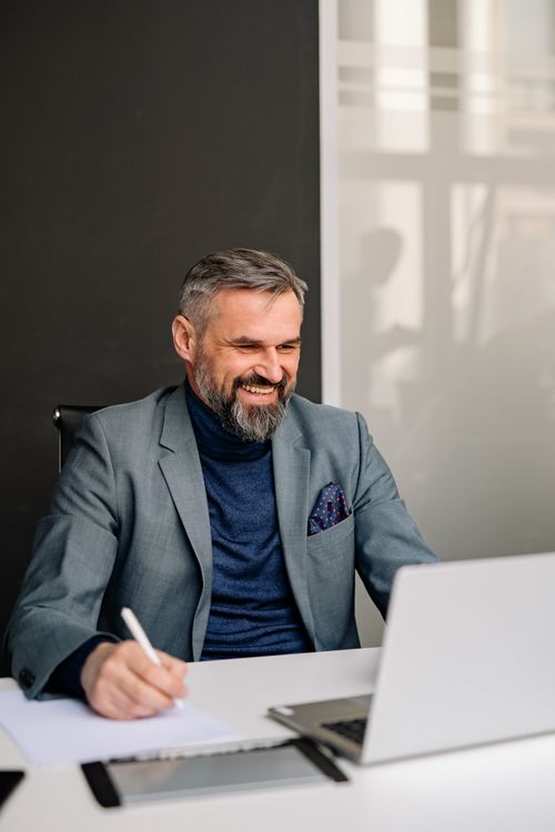 Free Businessman in gray suit smiling confidently while working in a modern office environment. Indoors, natural light. Stock Photo