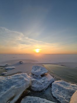 Beautiful icy seashore with a serene sunrise over the horizon, highlighting the winter landscape.