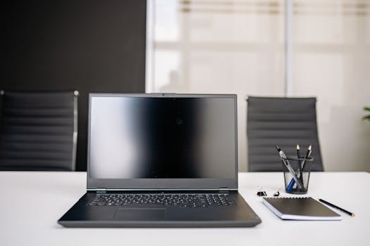 A sleek office setup featuring a laptop, notebooks, and chairs on a white desk.