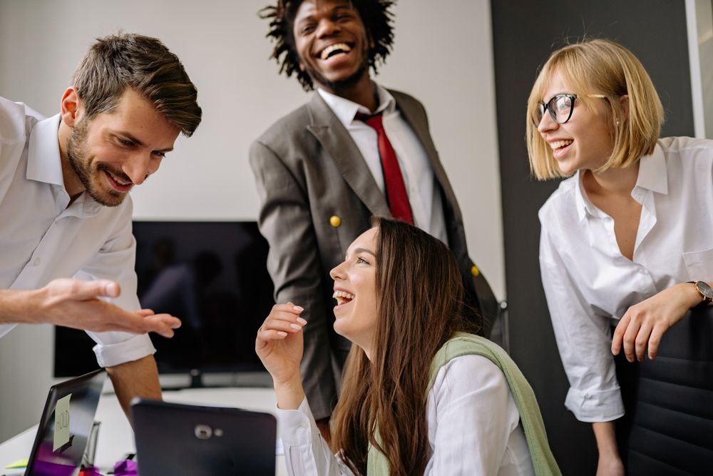 Four colleagues laughing together around a desk