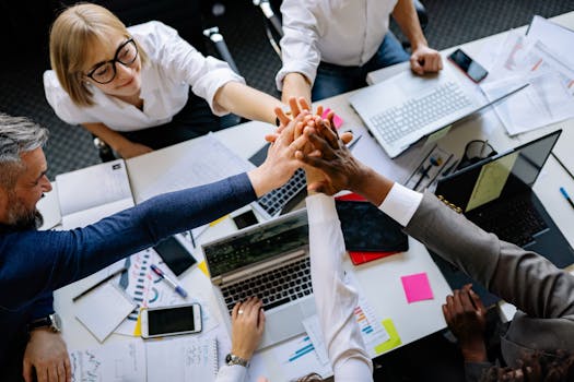 A group of diverse professionals high-fiving over a collaborative workspace.