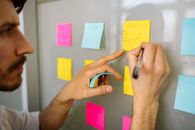 A Man Writing on a Yellow Sticky Note Posted on the White Wall