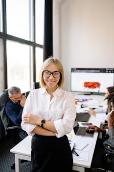 Professional businesswoman smiling in office setting with colleagues working in the background.