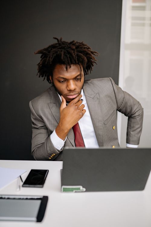 Free African American man in suit focused on laptop work, indoors office setting. Stock Photo