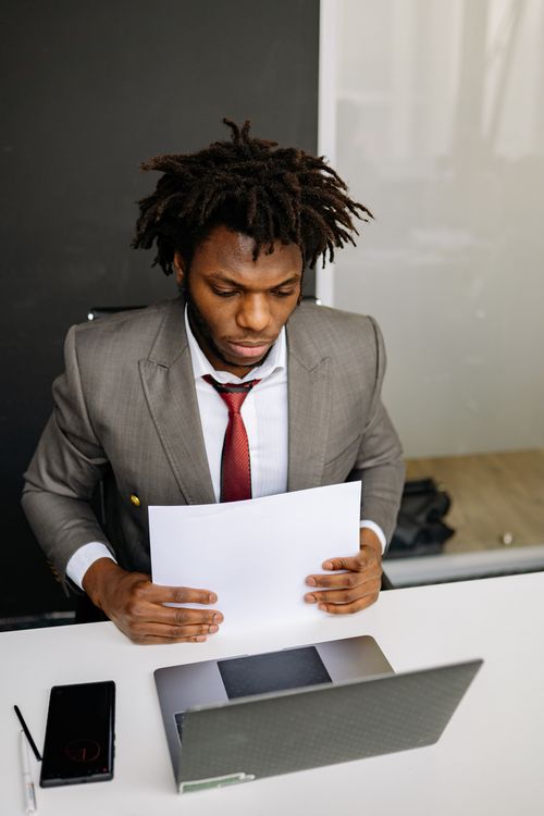 Free Businessman in formal suit reviewing document at office desk with laptop. Stock Photo