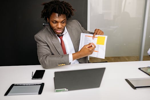 Businessman in formal attire presenting documents during an online meeting using a laptop.