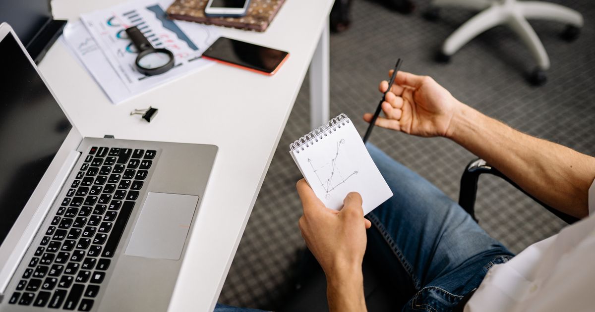 A job seeker at their laptop researching UX companies in the UK with a notepad by their side.