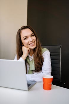Confident woman with laptop and coffee smiling in a stylish office environment.