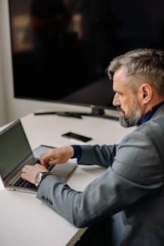 Focused adult businessman typing on a laptop at an office desk.