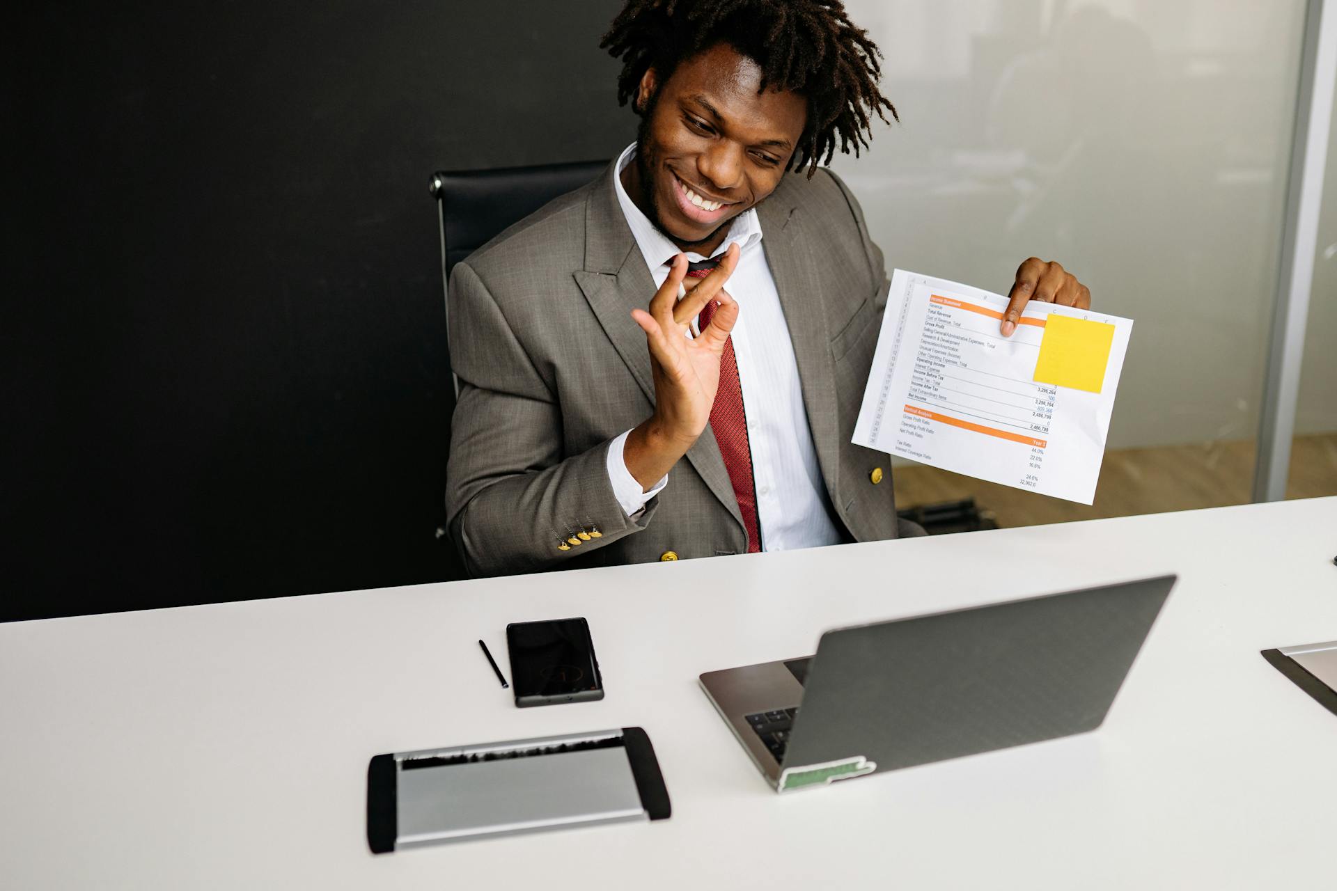 Smiling professional in a suit holds documents during a video call in an office setting.