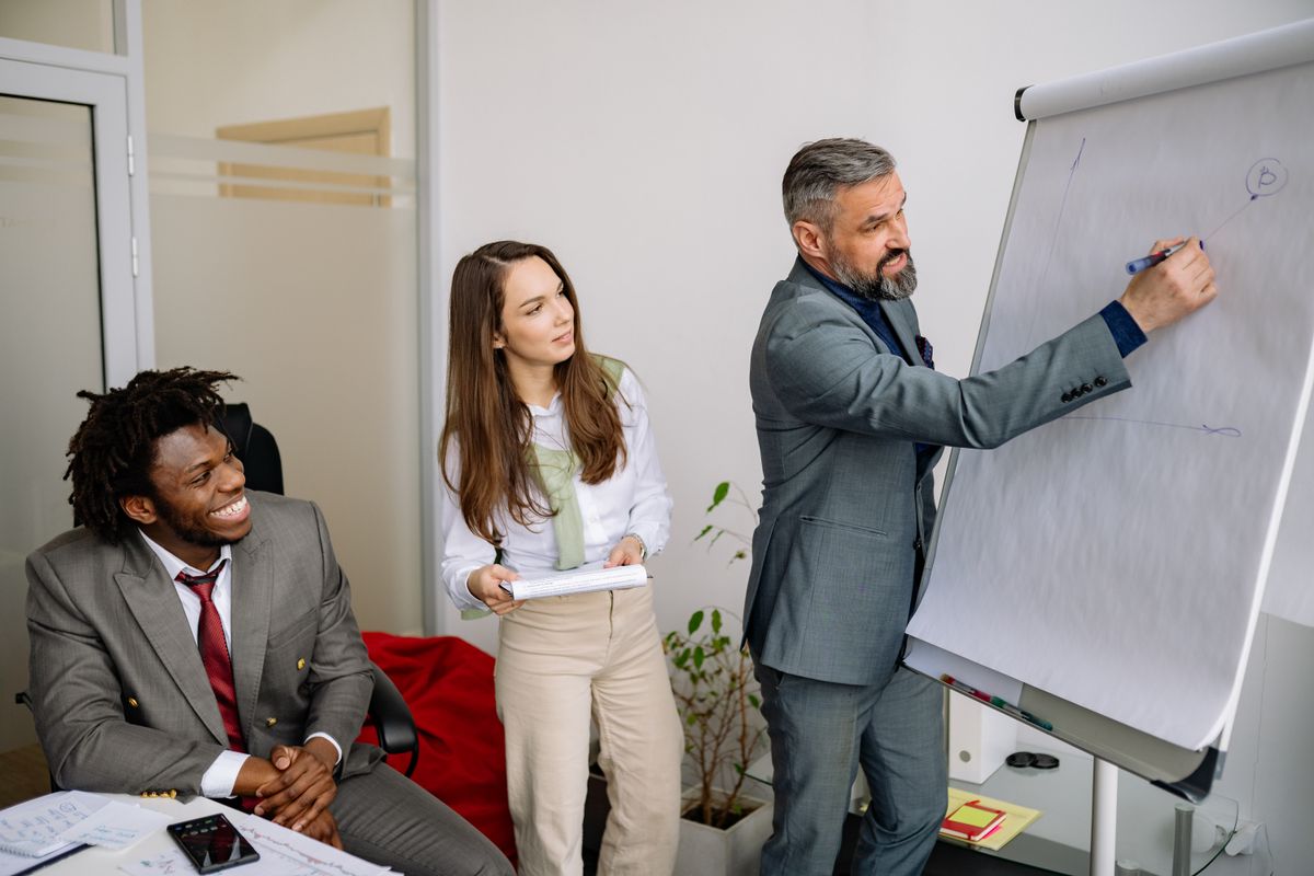 Un formateur explique un contenu au tableau à deux personnes lors de la conception d'un parcours