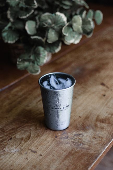 Close-up of an iced drink in a stainless steel cup on a rustic wooden table.