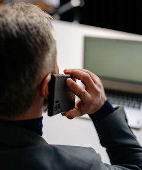Businessman making a phone call while working on a laptop at the office.
