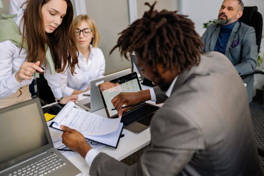 Professionals engaged in a collaborative meeting with laptops and documents in a conference room.