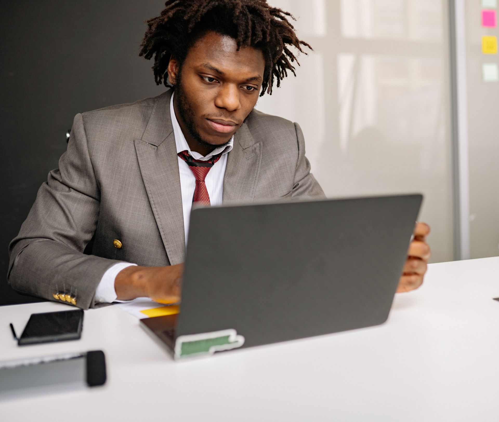 African American businessman focused on laptop work at a desk. Corporate attire in office setting.