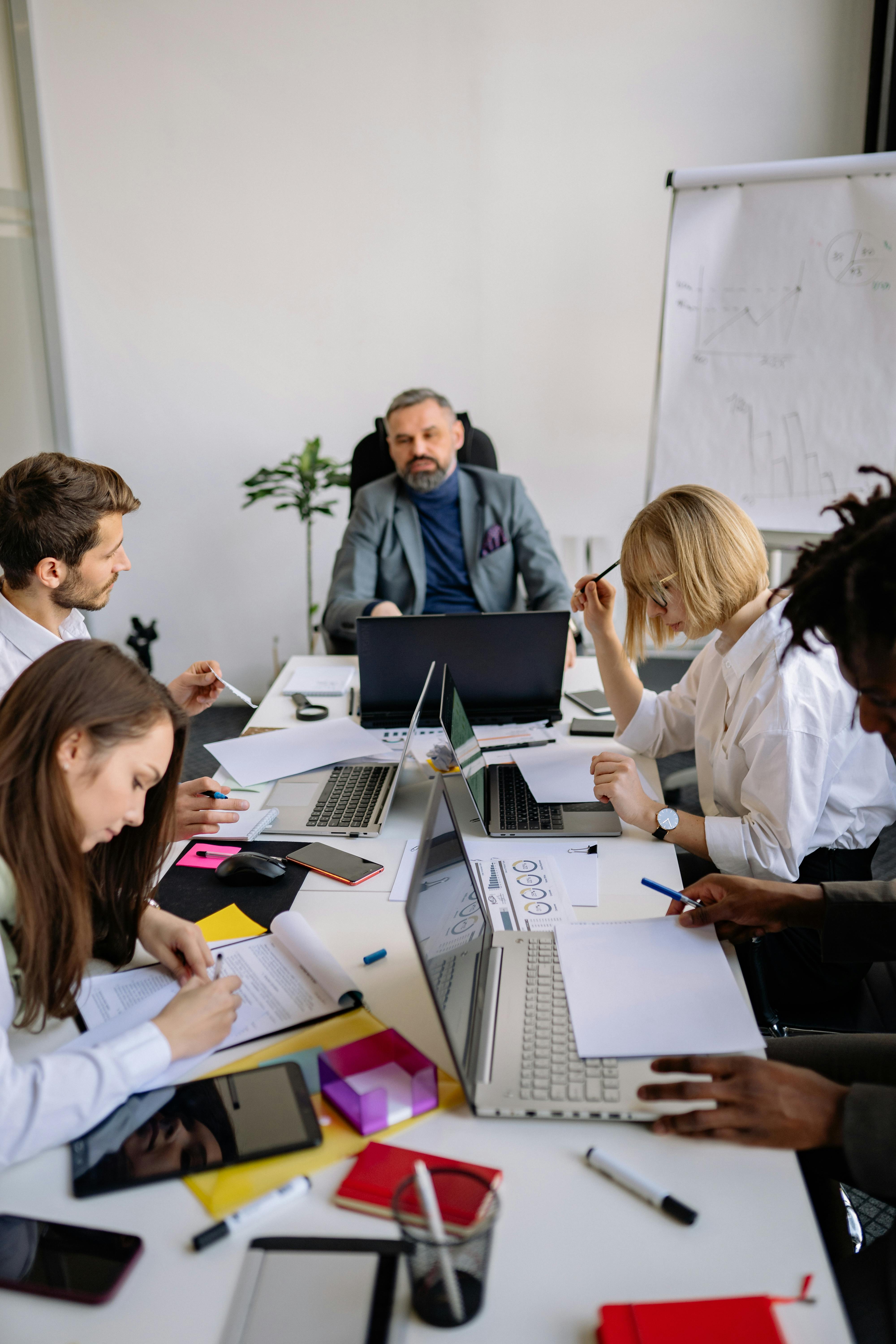 Group of colleagues brainstorming and planning in a modern office with laptops and documents.