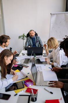 Group of colleagues brainstorming and planning in a modern office with laptops and documents.