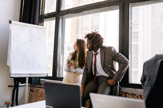 Two business professionals engaged in conversation near a presentation board in a modern office.