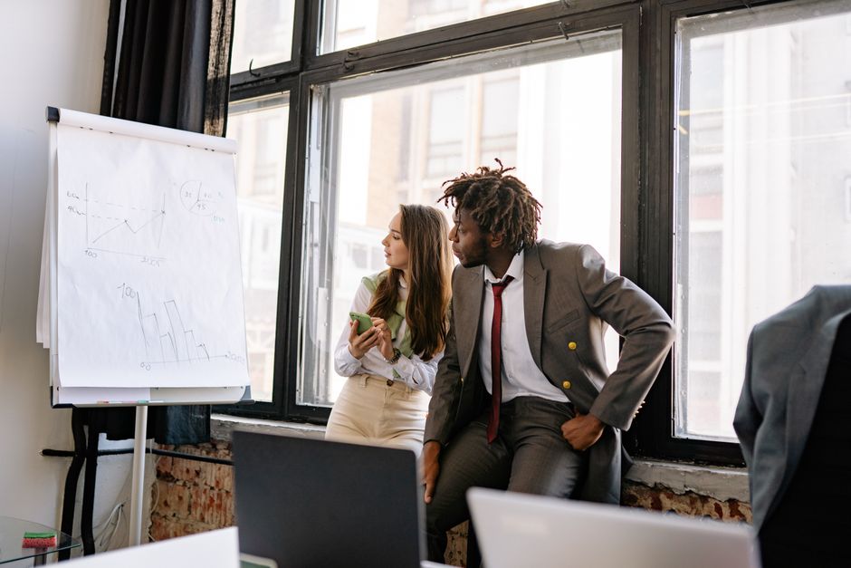 Photo by Yan Krukau on Pexels Two business professionals engaged in conversation near a presentation board in a modern office.