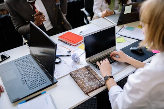 People discussing work on laptops during a team meeting in a modern office setting.