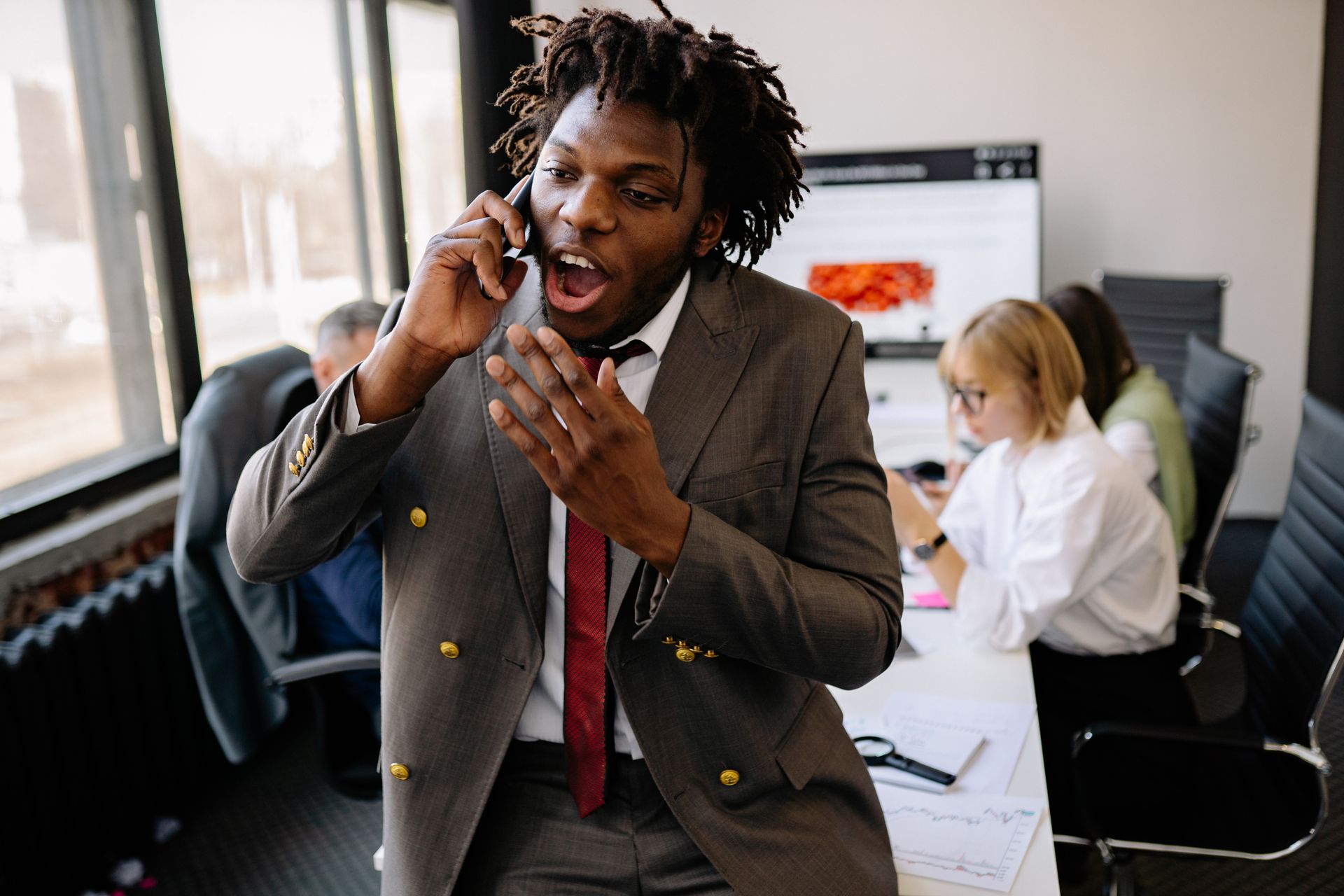 Energetic businessman in a suit having a phone call in a busy office environment.