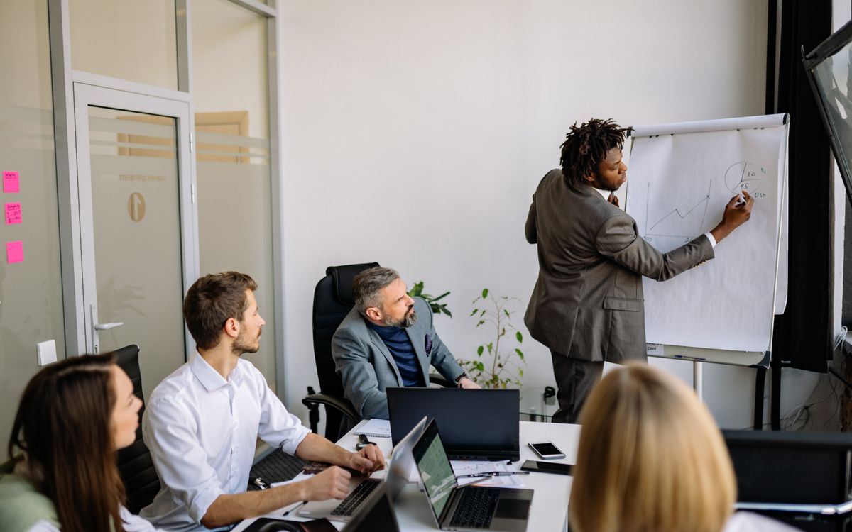 A diverse team in a modern office engaged in a strategic business meeting led by a presenter.
