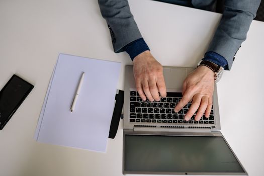 Overhead shot of a man in a suit typing on a laptop with a notepad and pen nearby.