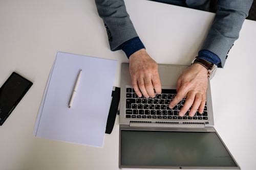 Free Overhead shot of a man in a suit typing on a laptop with a notepad and pen nearby. Stock Photo