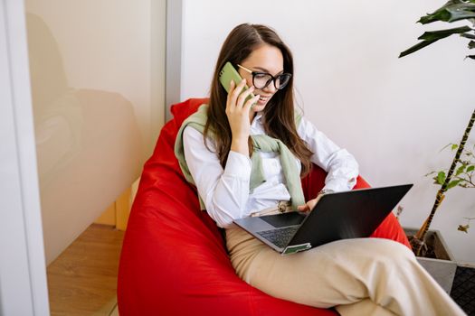 Businesswoman multitasking with laptop and smartphone in modern indoor setting.
