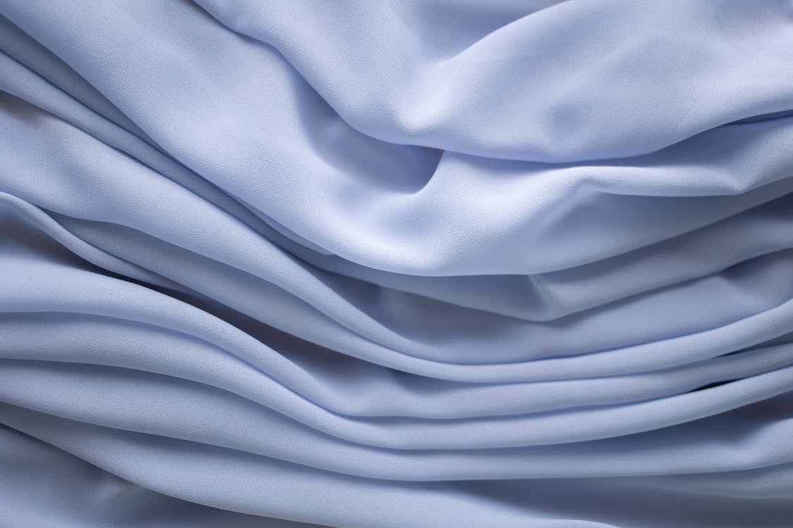 Closeup of textured background of crumpled light blue dyed textile with uneven texture
