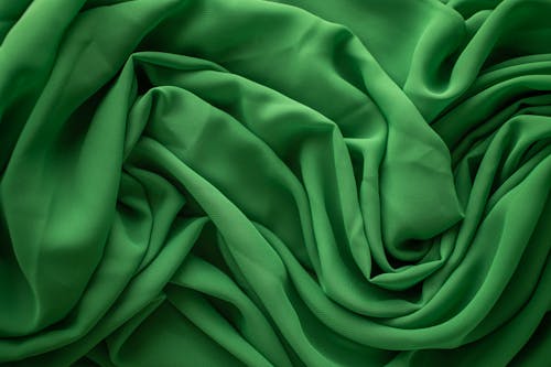 From above of textured background of creased green textile with uneven surface and wavy lines