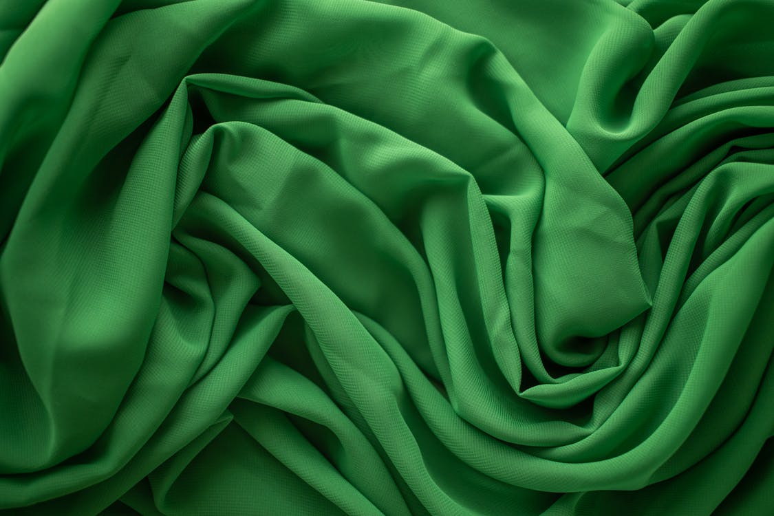 From above of textured background of creased green textile with uneven surface and wavy lines