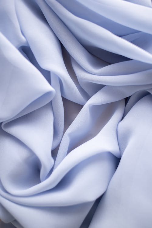 Abstract background representing crumpled light blue silk textile with uneven wavy thin texture