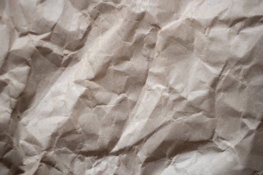 Textured background of crumpled thick paper surface of light brown color in daylight
