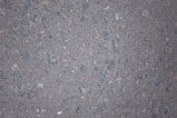 Top view of gray rough textured asphalt with stone inclusions scattered on surface