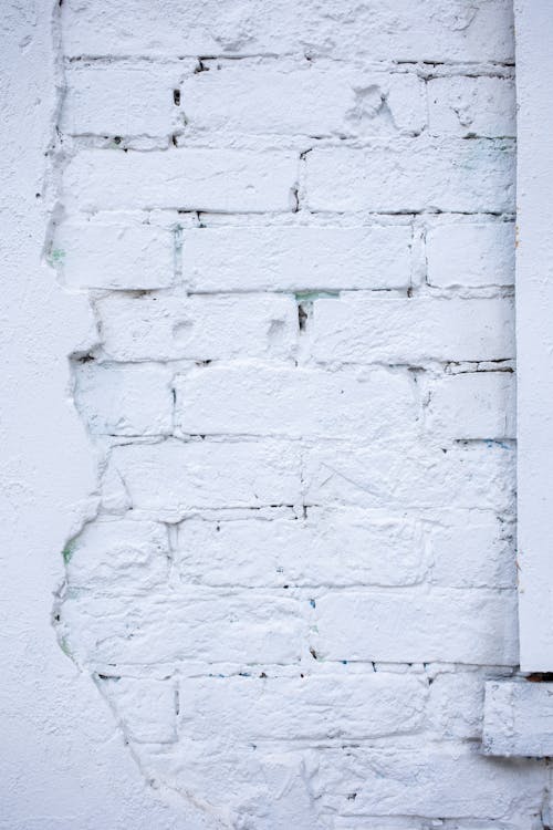 Shabby monochrome brick wall painted white with rough uneven surface and plaster remnants