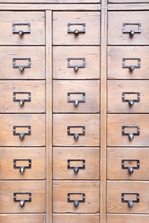 Surface of wooden cabinet with symmetrical rows of many drawers​ with metal handles