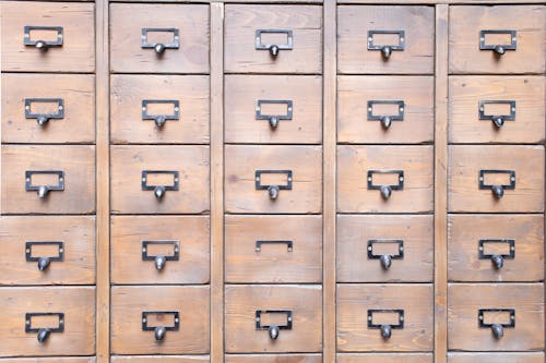 Background of wall full of many similar aged shabby vintage wooden drawers with metal round handles