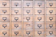 Background of wall full of many similar aged shabby vintage wooden drawers with metal round handles